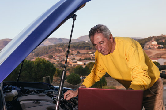 Senior man with laptop fixing car