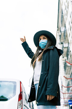 Young woman in the city wearing face mask and hailing a taxi cab