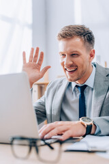 Smiling businessman having video call on laptop on blurred foreground in office