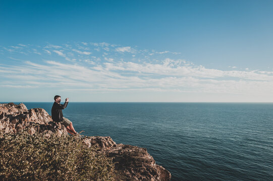 Young man taking photo of ocean from cliff in Sagres, Portugal