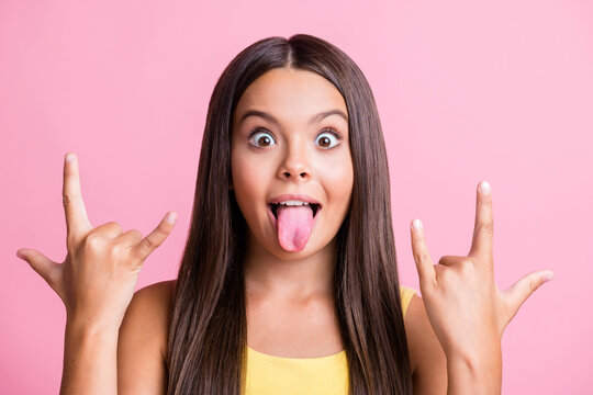 Photo of stylish trendy brown haired girl make horned sign stick-out tongue wear yellow singlet isolated on pink background