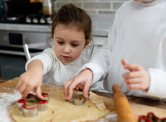 Children cut cookies from the dough. Brother and his sister cook cookies at home. A close-up portrait of a girl.