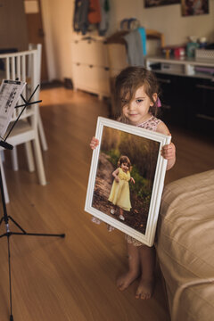 Young barefoot girl with wispy hair holding framed picture of herself