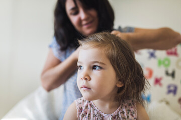 4 yr old girl with big brown eyes and smiling mom braiding her hair