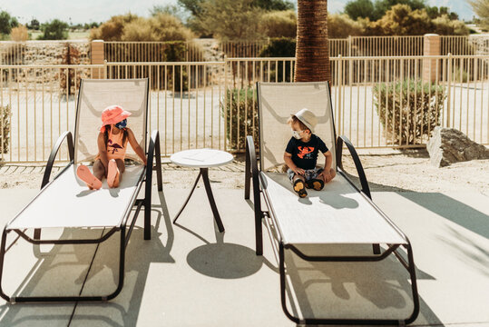 Young toddler siblings with mask on sitting by pool in Palm Springs
