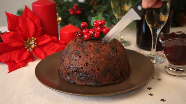 Woman hand cut a Christmas pudding with holly on top.