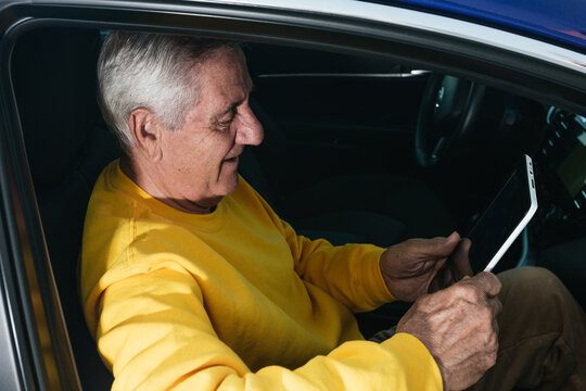 Elderly man smiling while sailing on a tablet in a vehicle