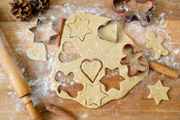 Still life, a top view of a kitchen board with rolled out dough, raw gingerbread preparations and cinnamon sticks. Top of the spruce cones.