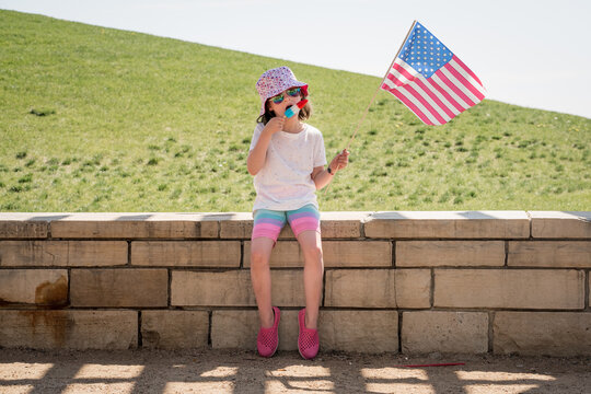 young girl holds an American flag while eating a red and blue popsicle