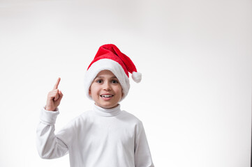 The boy in the red santa hat smiles and points his finger up. Christmas concept.