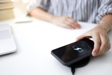 Charging mobile phone battery with wireless charging device in the table. Smartphone charging on a charging pad