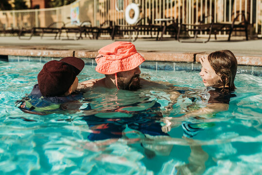 Funny image of dad in child's hat playing in the pool with sons