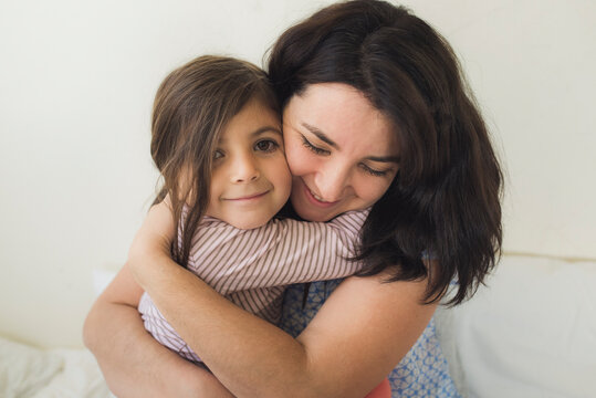 Smiling mid-30's mother hugging happy 6 yr old daughter