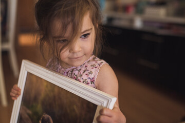 Sweet brown-eyed 4 yr old girl with wispy hair holding framed picture