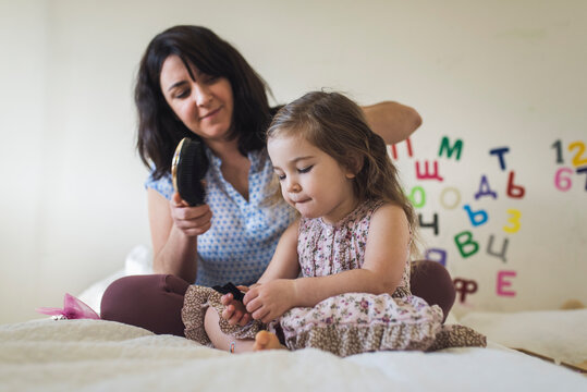 Mother brushing 4 yr old daughter's hair while sitting on bed