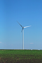 Fototapeta premium Aerogenerador eléctrico entre campos de cultivo en Rumanía. Aerogenerador con un cielo azul de fondo.