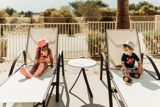 Young toddler siblings with mask on sitting by pool in Palm Springs