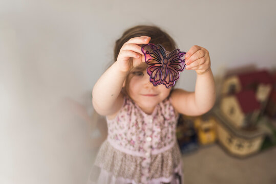 4 yr old girl in sleeveless dress examining butterfly suncatcher