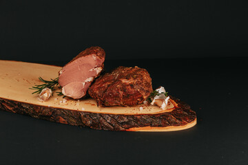 Smoked pork muscles and bacon on a wooden board with the addition of fresh aromatic herbs, garlic, sea salt and pepper.