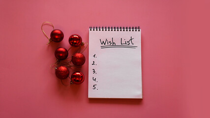 Notebook on pink background with christmas balls - new year wish list. Top view