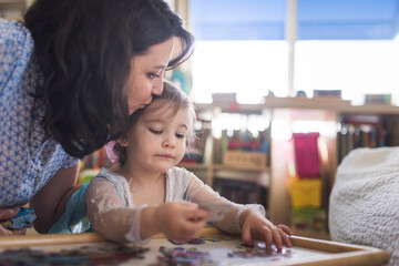 Mid-30's mom kissing head of 4 yr old daughter putting puzzle together