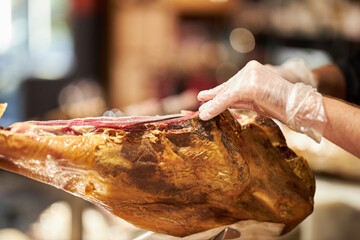 The chef is cutting the jamon. image of a ham cutter with a knife cutting a thin slice of ham. Dry Spanish ham, Jamon Serrano, Bellota, Italian Prosciutto Crudo or Parma ham.