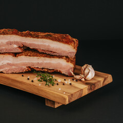 Smoked pork muscles and bacon on a wooden board with the addition of fresh aromatic herbs, garlic, sea salt and pepper.