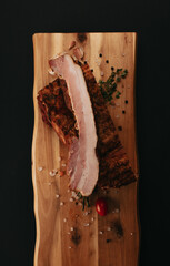 Smoked pork muscles and bacon on a wooden board with the addition of fresh aromatic herbs, garlic, sea salt and pepper.