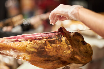 The chef is cutting the jamon. image of a ham cutter with a knife cutting a thin slice of ham. Dry Spanish ham, Jamon Serrano, Bellota, Italian Prosciutto Crudo or Parma ham.