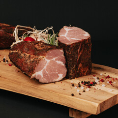 Smoked pork muscles and bacon on a wooden board with the addition of fresh aromatic herbs, garlic, sea salt and pepper.