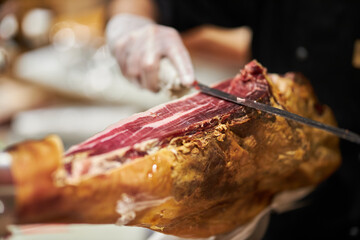 The chef is cutting the jamon. image of a ham cutter with a knife cutting a thin slice of ham. Dry Spanish ham, Jamon Serrano, Bellota, Italian Prosciutto Crudo or Parma ham.