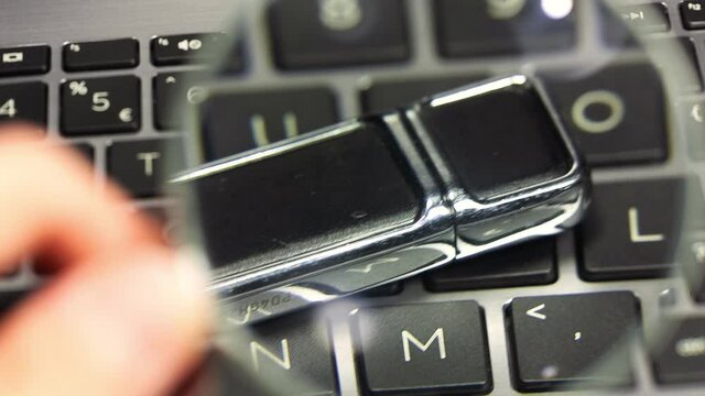 Hand holding a magnifying glass inspecting, examining an usb flash drive, memory stick, closeup. Data storage device investigation, searching for private files, hacking, loupe file search concept