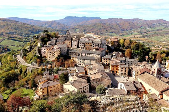High angel view of beautiful small old town on the hill surrounded by mountains and colorful autumn trees against nice blue and clouds sky during autumn in Pennabilli,Province of Rimini,Italy
