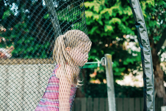 Young girl with grumpy face leaning on trampoline netting
