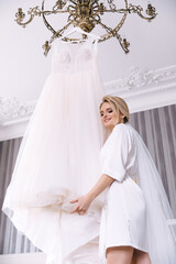 happy bride hugs her beautiful and delicate white dress that hangs on a hanger