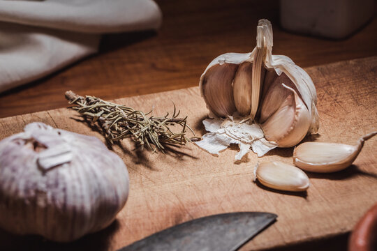 Garlic head and cloves on wooden board next to rosemary branches - Powered by Adobe