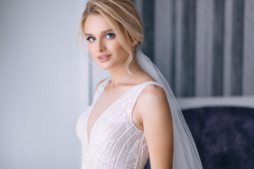 beautiful bride with blonde hair in elegant wedding dress posing in the room on wedding morning