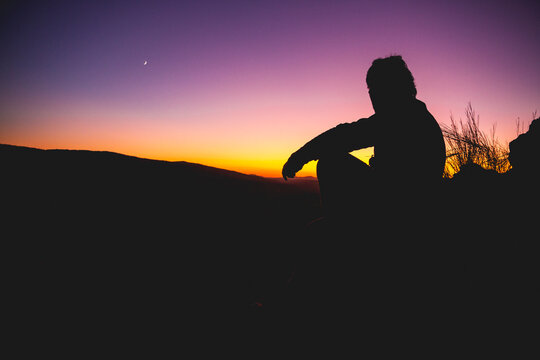 Silhouette of man looking with binoculars at sunset with the moo