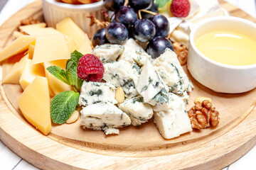 Board with different types of cheese. Cheeses mix set dor blu chedar parmesan brie honey sauce finger bread and grape on wooren palte. Restaurant menu breakfast plate. Healthy snack assortment.