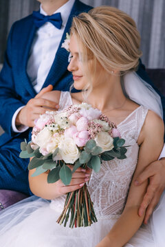 the bride in a white dress holds a bouquet, the groom in a blue suit holds the girl's hand on the shoulder hugging her.