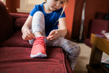 Young girl sitting on sofa and tying a shoe lace on her sneaker