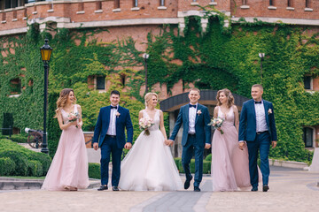 Newlyweds and their smiling friends walk near the castle.