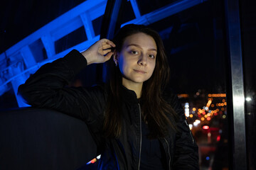 Young happy woman sitting in ferris wheel booth riding on attraction, blue light