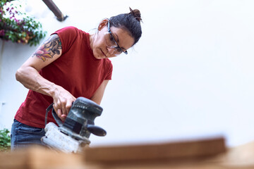 Young woman polishing a wooden plank with a power sander
