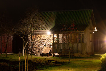 Wooden bathhouse with dry birch firewood in the garden under the light of street lamps