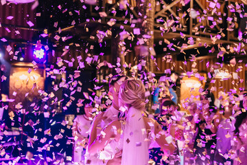 A touching and emotional dance of a couple at their wedding with confetti and colorful lights on the background.