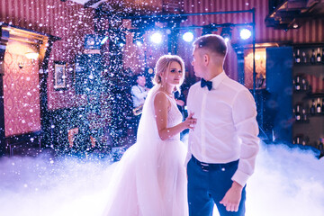 Newly married couple dancing on their wedding party with heavy smoke and multicolored lights on the...