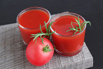 Tomato juice in a glass glass and fresh tomato on a wooden background.