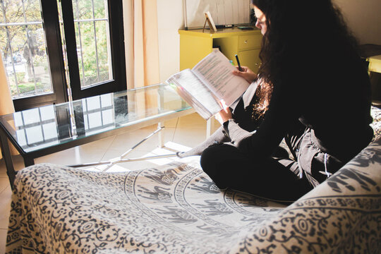woman reading and underlining a book on the sofa