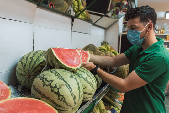 A young man wearing a mask placing watermelons in the fruit shop.